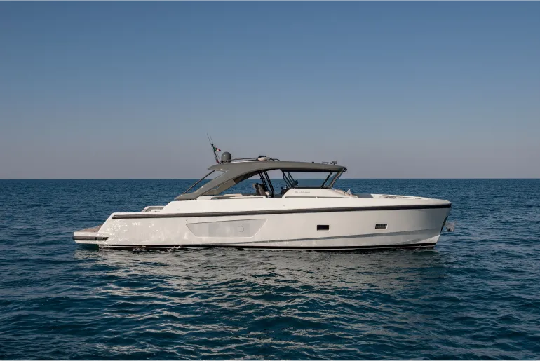 Side profile view of the Bluegame BG54 yacht at sea, showcasing its sleek white hull, tinted windows, and streamlined hardtop under a clear blue sky.